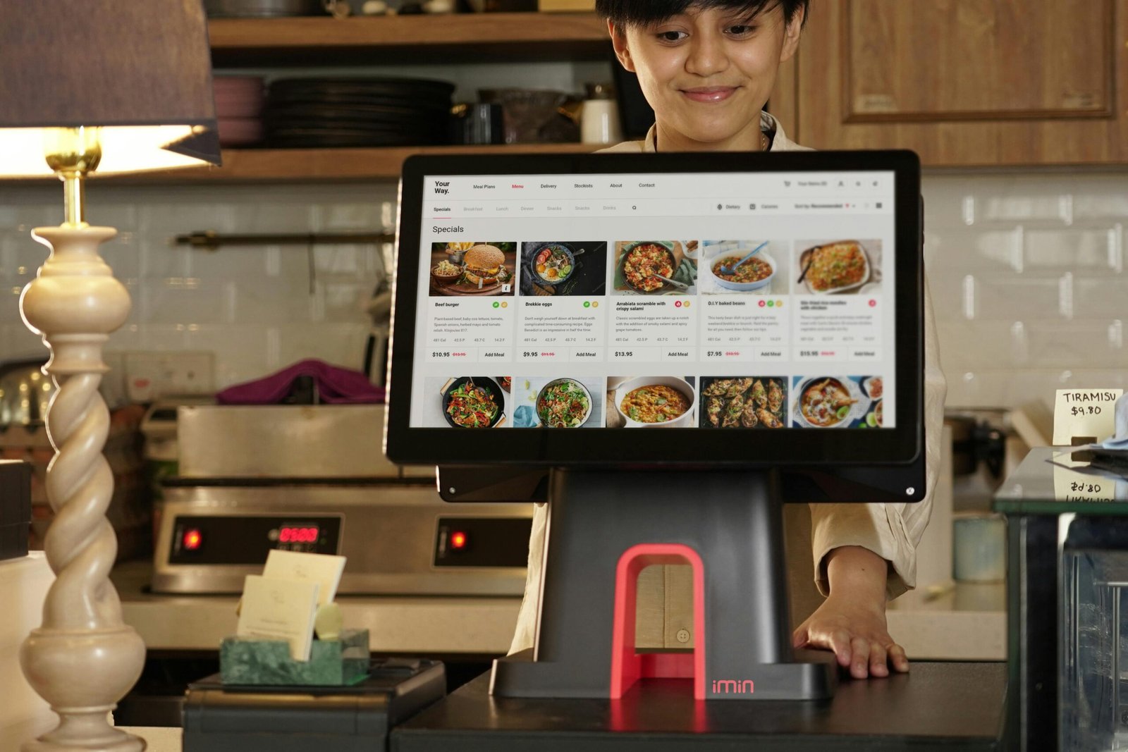 pexels-photo-12935053-12935053 A cashier uses a touchscreen system for taking orders in a restaurant setting.